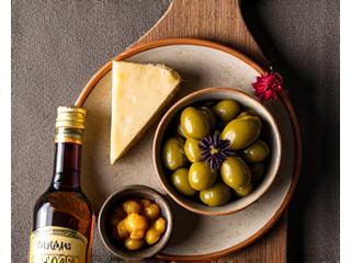 Una variedad de alimentos fermentados tradicionales españoles o mediterráneos como aceitunas, queso curado artesanal, vinagre de Jerez y verduras encurtidas en recipientes de cerámica.